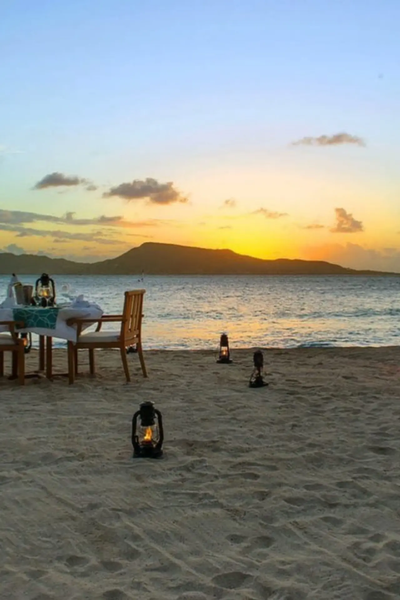 Private beach dinner setup at sunset with lanterns on the sand in the Grenadines